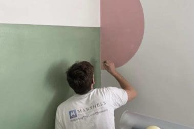 Painter applying green and pink paint to a wall with a brush