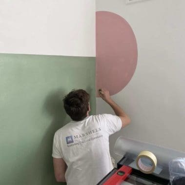 Painter applying green and pink paint to a wall with a brush